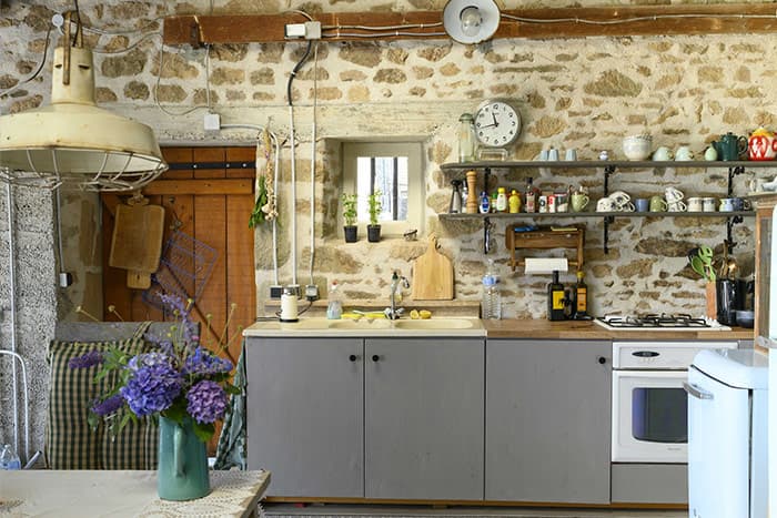 Rustic kitchen with exposed stone walls, open shelving, and hydrangeas
